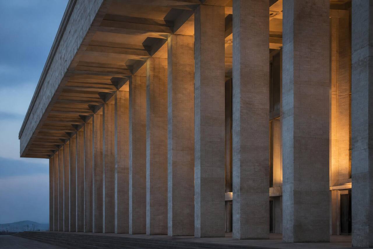 Stone colonnade of an institutional building at dusk, lit from within